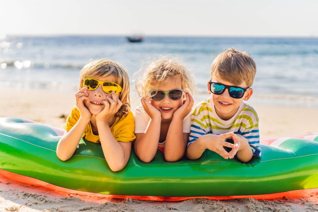Tres niños sonrientes mirando a cámara en la playa durante el verano